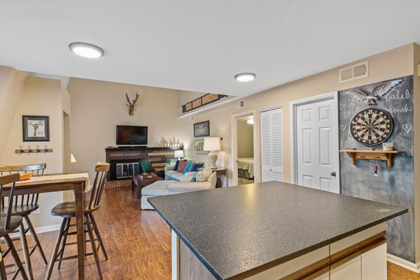 A spacious living room with a fireplace, a dining area with wooden chairs, and a kitchen with a large island.