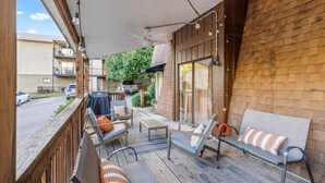 A covered outdoor seating area with wooden flooring, a barbecue grill, and a view of a residential street.