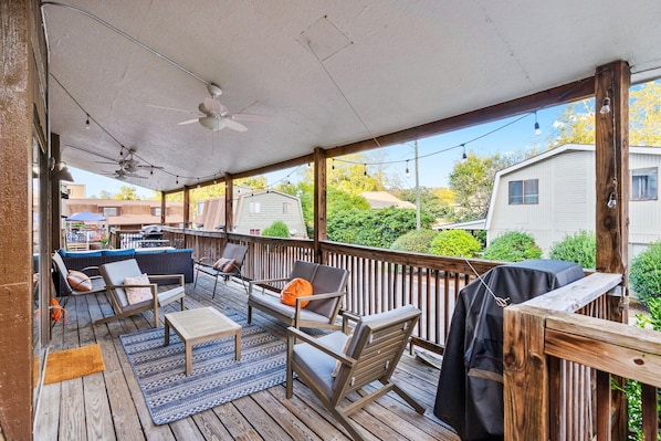 Eine überdachte Terrasse im Freien mit Holzmöbeln, einem Deckenventilator und Lichterketten.