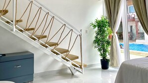 Una habitación de hotel moderna con una escalera, una planta en maceta, una cama y vistas a una piscina.