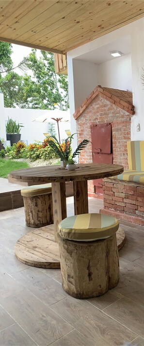 Un espace extérieur aménagé dans un style rustique, avec une table et des tabourets en bois, une cheminée en briques et des plantes en pot.