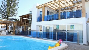 Un hotel moderno con piscina, una pérgola de madera y vistas despejadas del entorno.