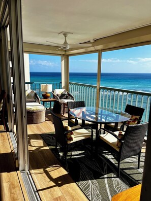Un balcon avec une table en verre, des fauteuils en osier, un canapé et une vue sur l’océan.