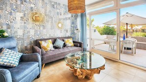 Ein modernes Wohnzimmer mit einem grauen Sofa, gemusterten Kissen, einem Glastisch und einer Wandverzierung.