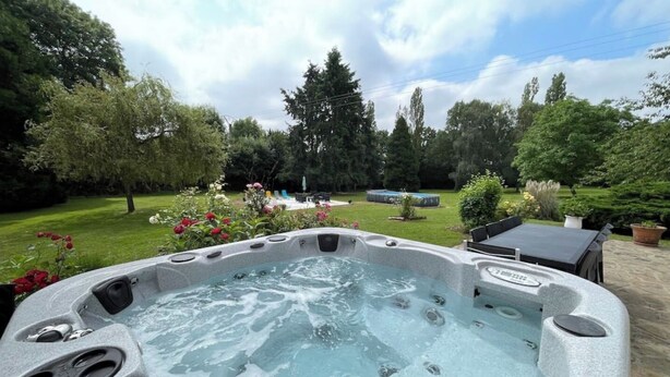 A hot tub in a backyard with a lawn, trees, and a table. - Large villa in the heart of the Parc du Perche (Nogent-le-Rotrou)