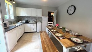 A modern kitchen with white cabinets, a wooden dining table set for four, and a clock on the wall. - Large villa in the heart of the Parc du Perche (Nogent-le-Rotrou)