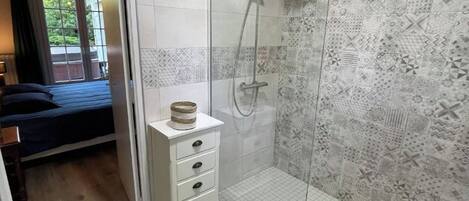 A modern bathroom with a glass shower enclosure, a white sink, and a wooden bedside table.
