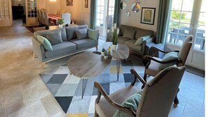 A spacious living room with a high ceiling, exposed wooden beams, a large sofa, a coffee table, and a dining area in the background. - Large villa in the heart of the Parc du Perche (Nogent-le-Rotrou)