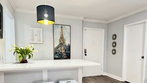 Una cocina moderna con encimera blanca, dos taburetes blancos, una lámpara colgante y un cuadro de la Torre Eiffel.