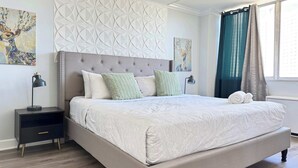 Un dormitorio con una cama grande, una mesita de noche, una lámpara de pared y una obra de arte.