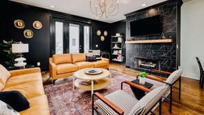 Ein modernes Wohnzimmer mit Schwarz-Gold-Farbschema, das ein Ledersofa, einen runden Couchtisch und einen Kamin zeigt.