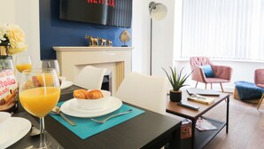 A modern living room with a flat-screen TV displaying 'NETFLIX', a dining area with breakfast items, and a cozy seating arrangement. - Tudors eSuites Four Bedroom House Garden (Coventry)