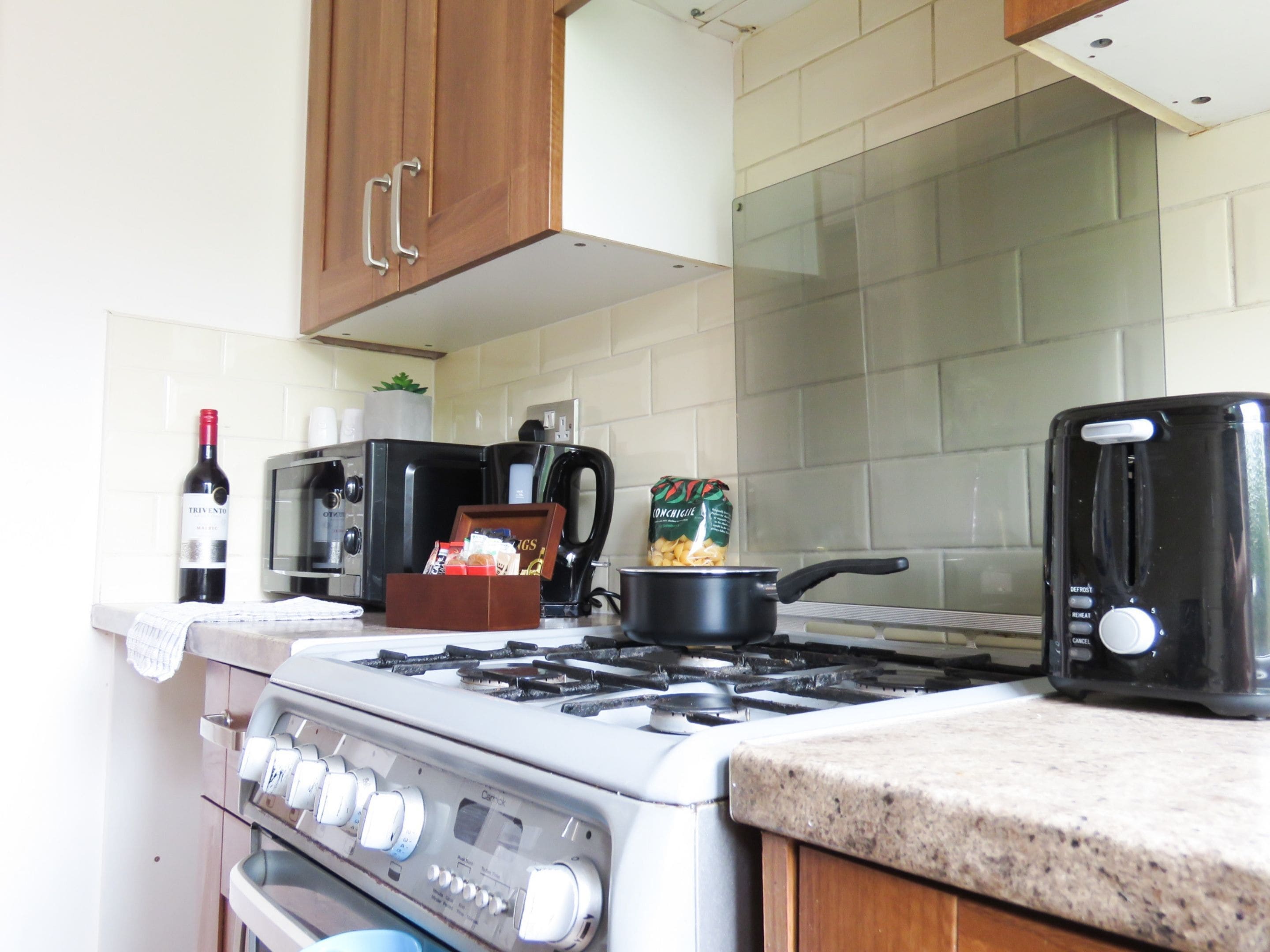 A kitchen with a gas stove, a coffee maker, a toaster, and a bag of pasta.
