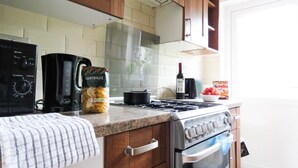 A kitchen with wooden cabinets, a gas stove, an oven, a coffee maker, a bottle of wine, and a bag of pasta. - Tudors eSuites Four Bedroom House Garden (Coventry)
