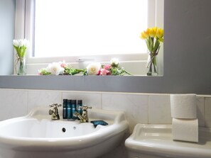 A bathroom with a white sink, a toilet, and a window above the sink. There are flowers in a vase on the windowsill. - Tudors eSuites Four Bedroom House Garden (Coventry)