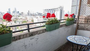 A balcony with a view of a cityscape, a small table, and potted red flowers. - Stylish flat near London Bridge with balcony views - Pass the Keys (London)