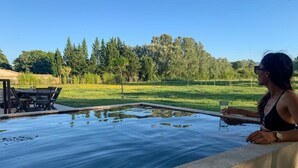 Une personne se détend au bord d’une piscine, avec vue sur un champ verdoyant et des arbres.