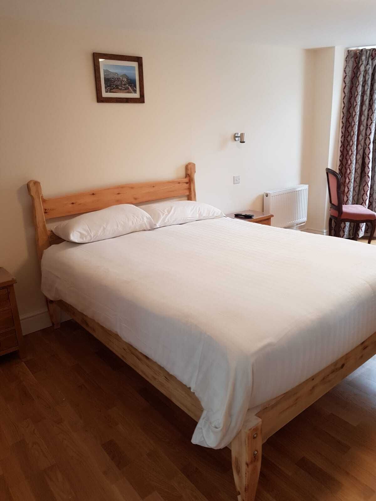 Une chambre à coucher avec un lit en bois, une table de chevet, une chaise et un radiateur.