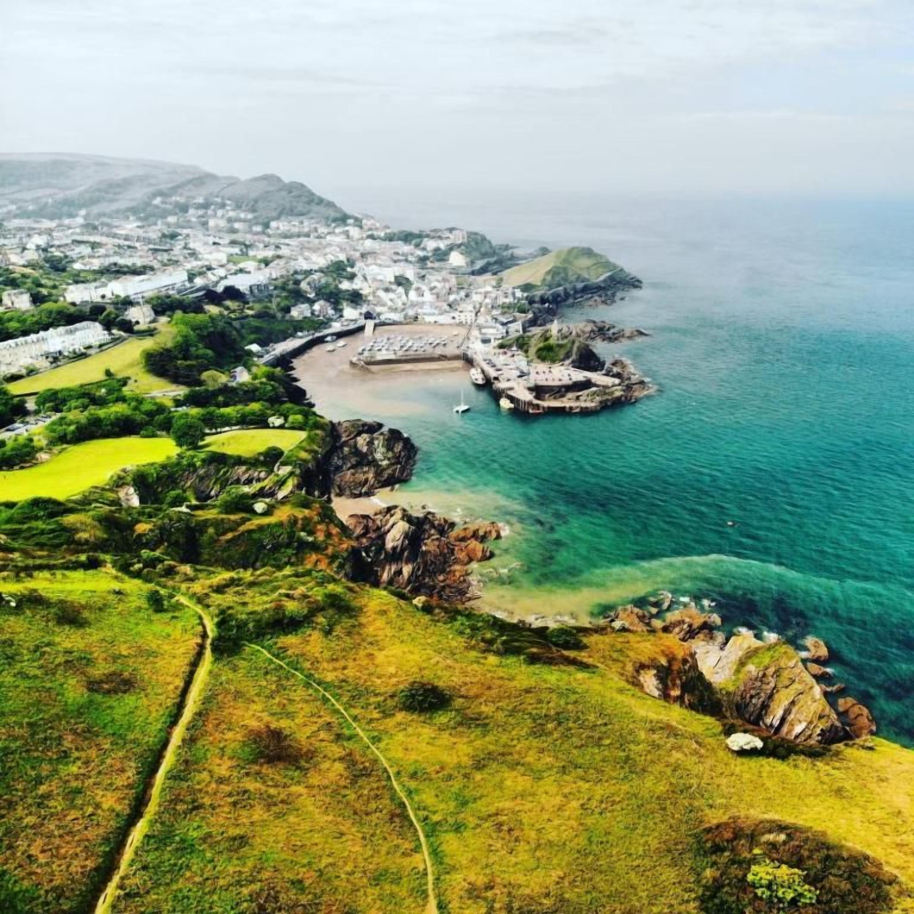 An aerial view of a coastal town with a prominent rocky peninsula, a marina, and a golf course.