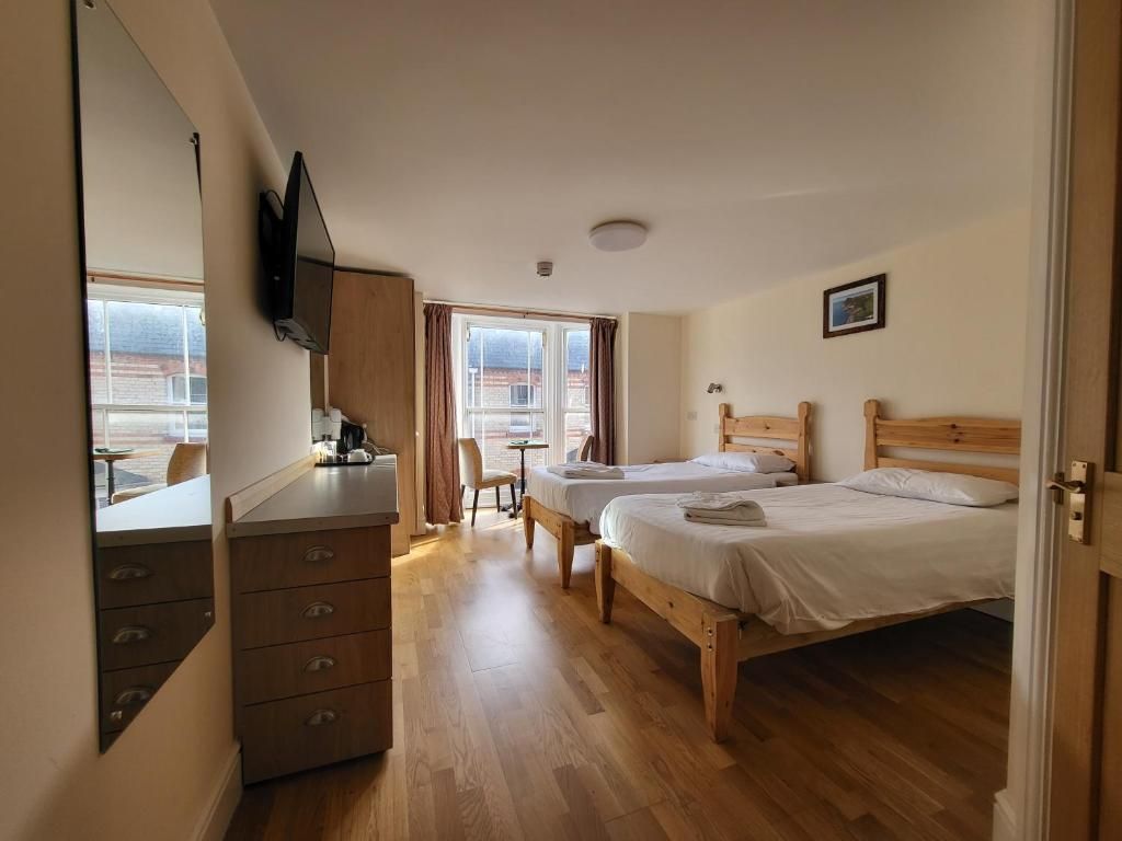 A hotel room with two wooden beds, a desk with a chair, a small table, and a window with curtains.