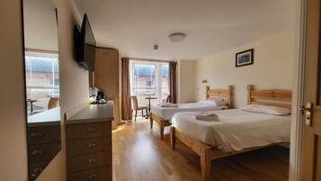 A hotel room with two wooden beds, a desk with a chair, a small table, and a window with curtains.