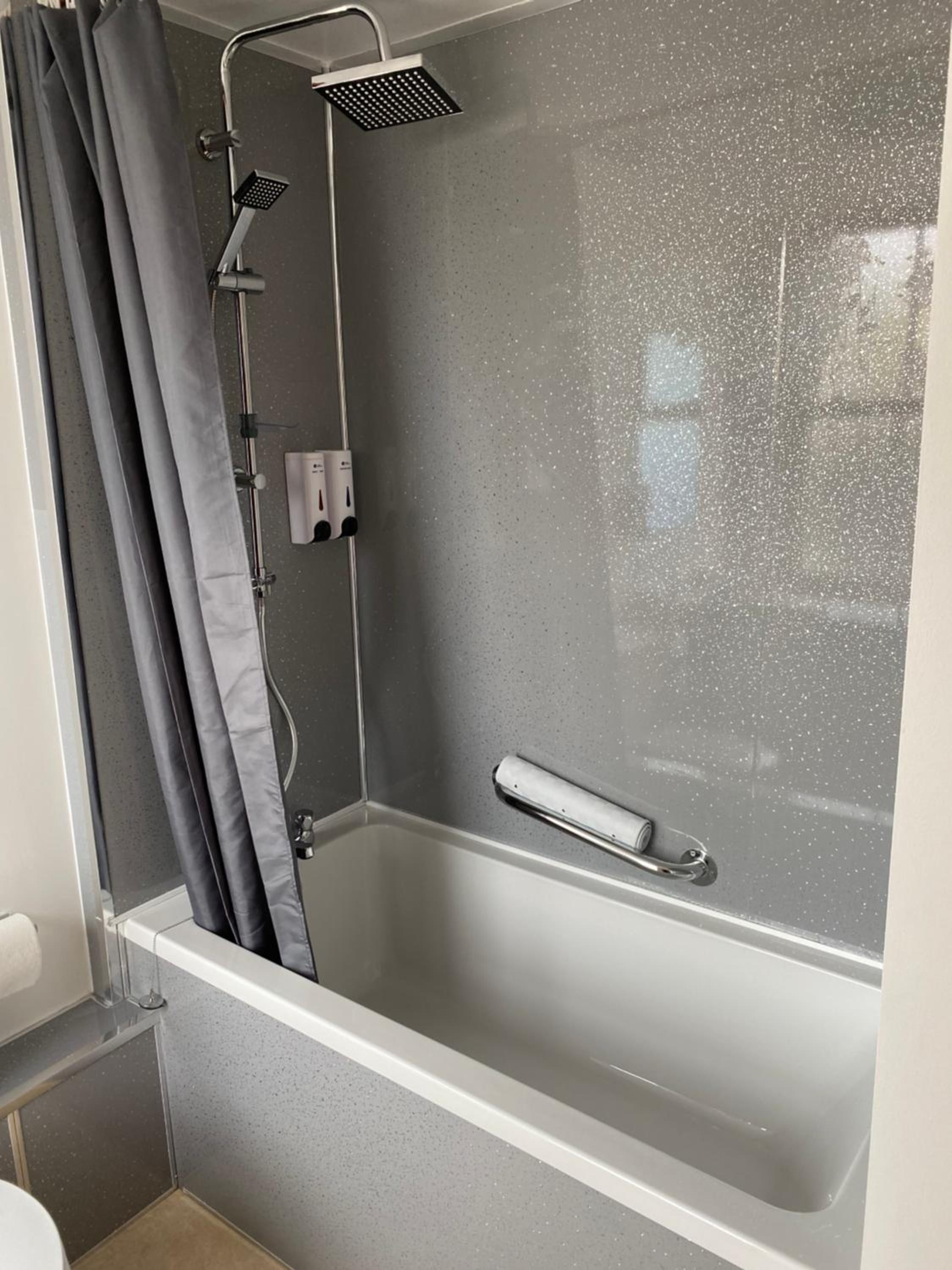 A modern shower enclosure with a handheld showerhead and a wall-mounted control panel.