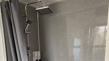 A modern shower enclosure with a handheld showerhead and a wall-mounted control panel.