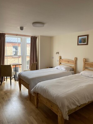 A room with two wooden beds, a chair, a table, and a window with curtains. - The Grand Harbour Hotel (Ilfracombe)