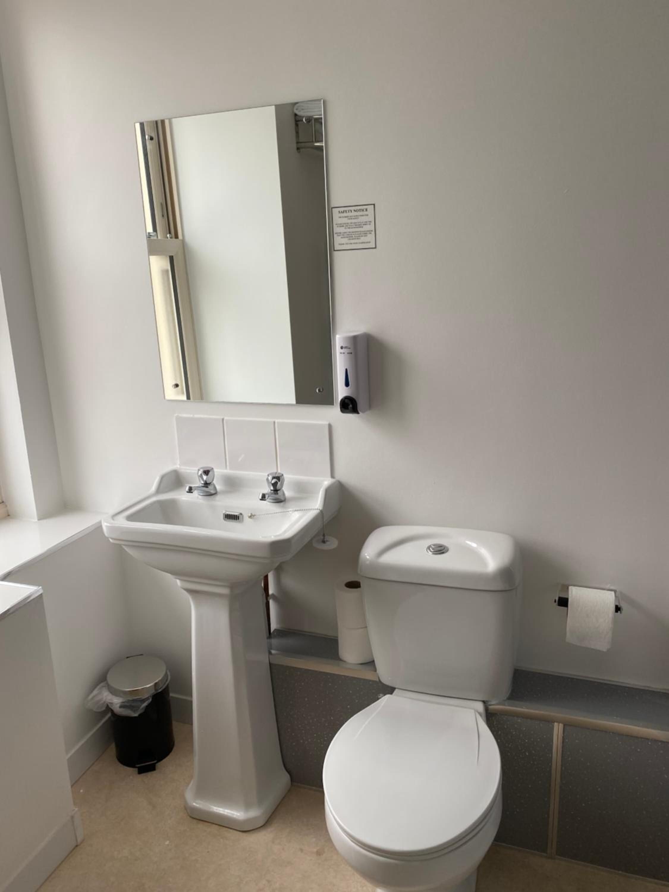 A bathroom with a pedestal sink, toilet, and a mirror.