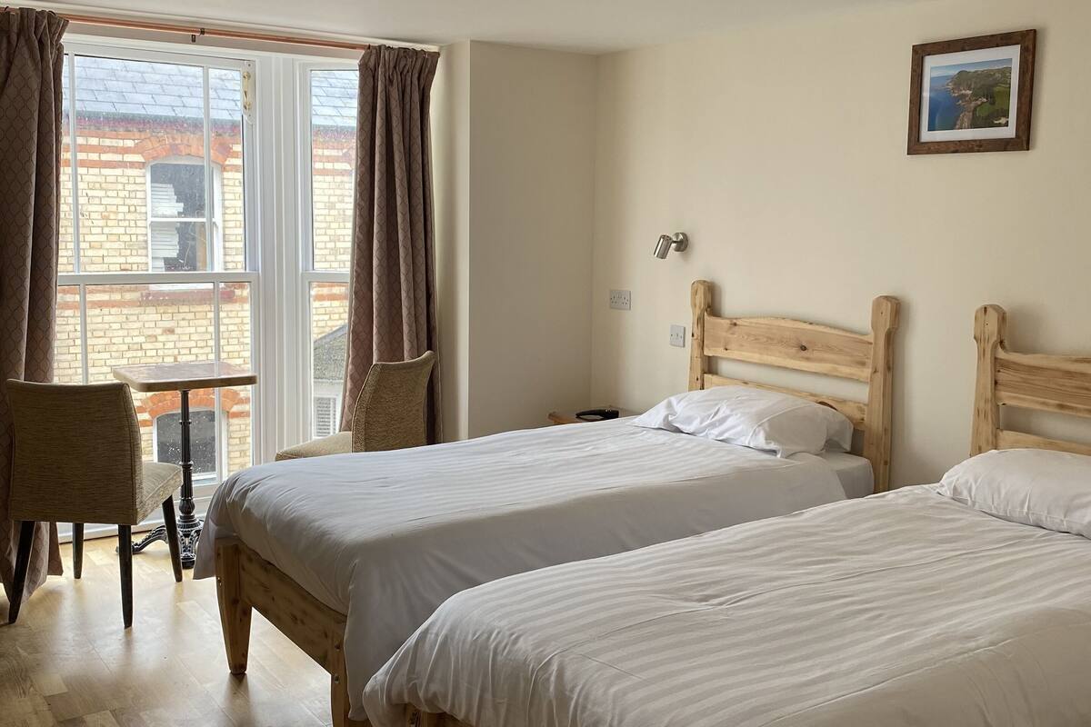 Ein Zimmer mit zwei Holzbett, einem Stuhl, einem Tisch und einem Fenster mit Vorhängen.