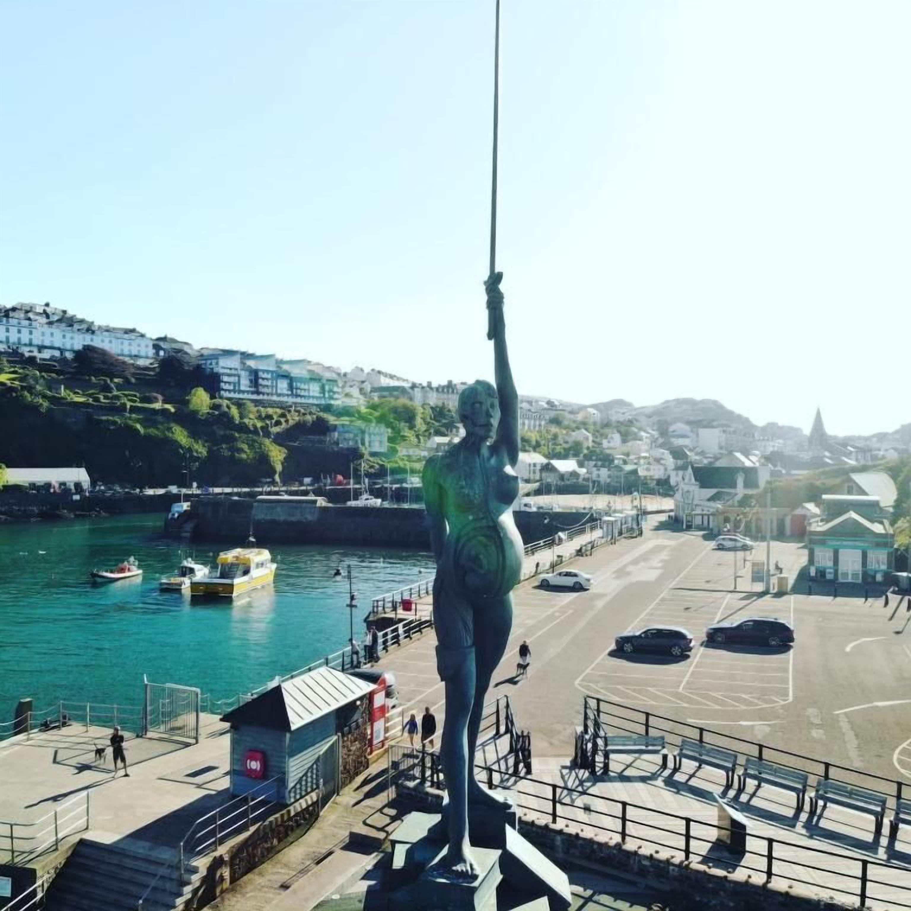 A statue of a woman holding a rope on a pier with a view of the harbor and buildings in the background.