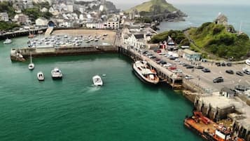 Un pueblo costero con un puerto deportivo, barcos y una colina destacada.
