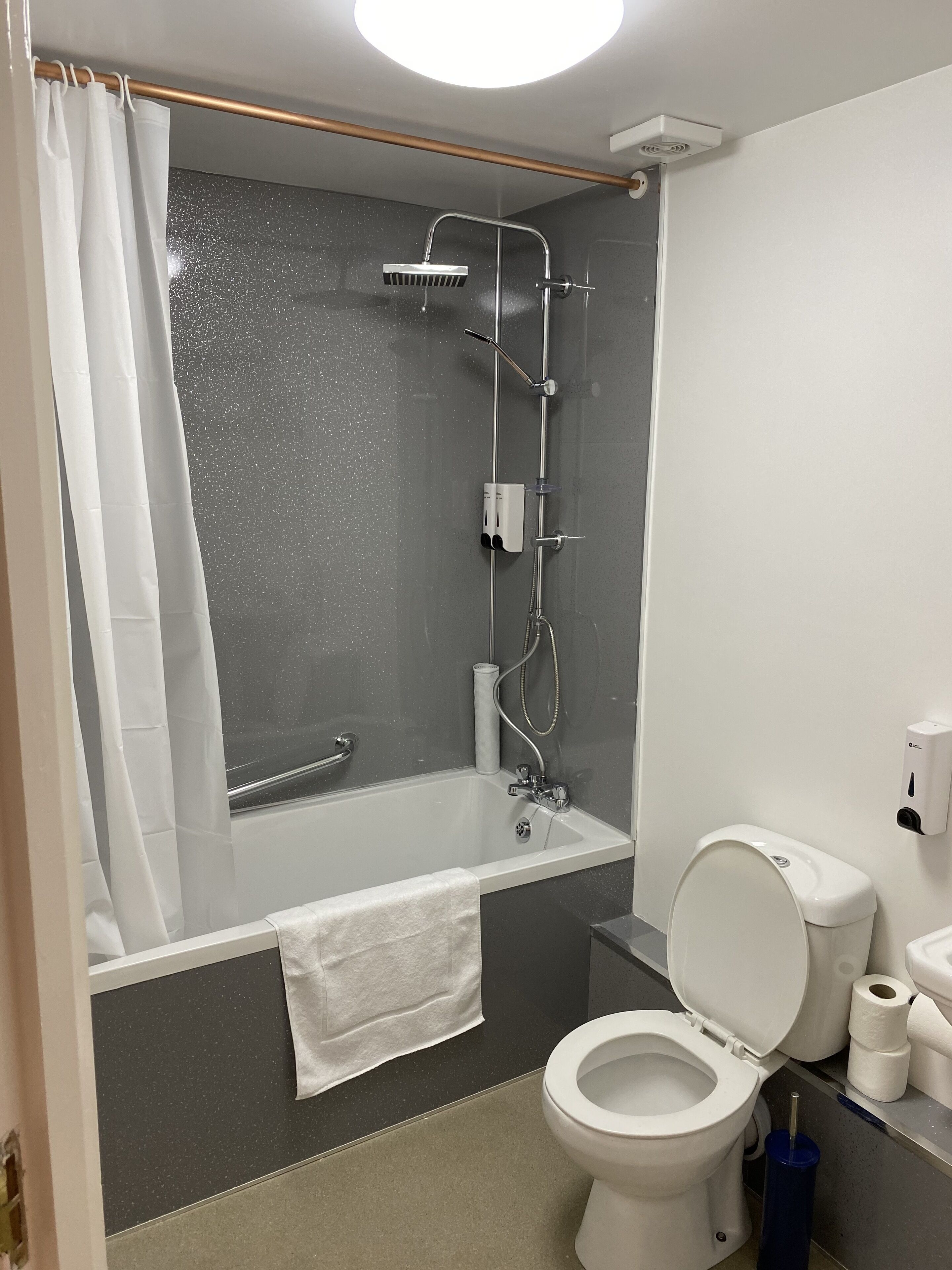 A modern bathroom with a bathtub, shower, toilet, and hand dryer.