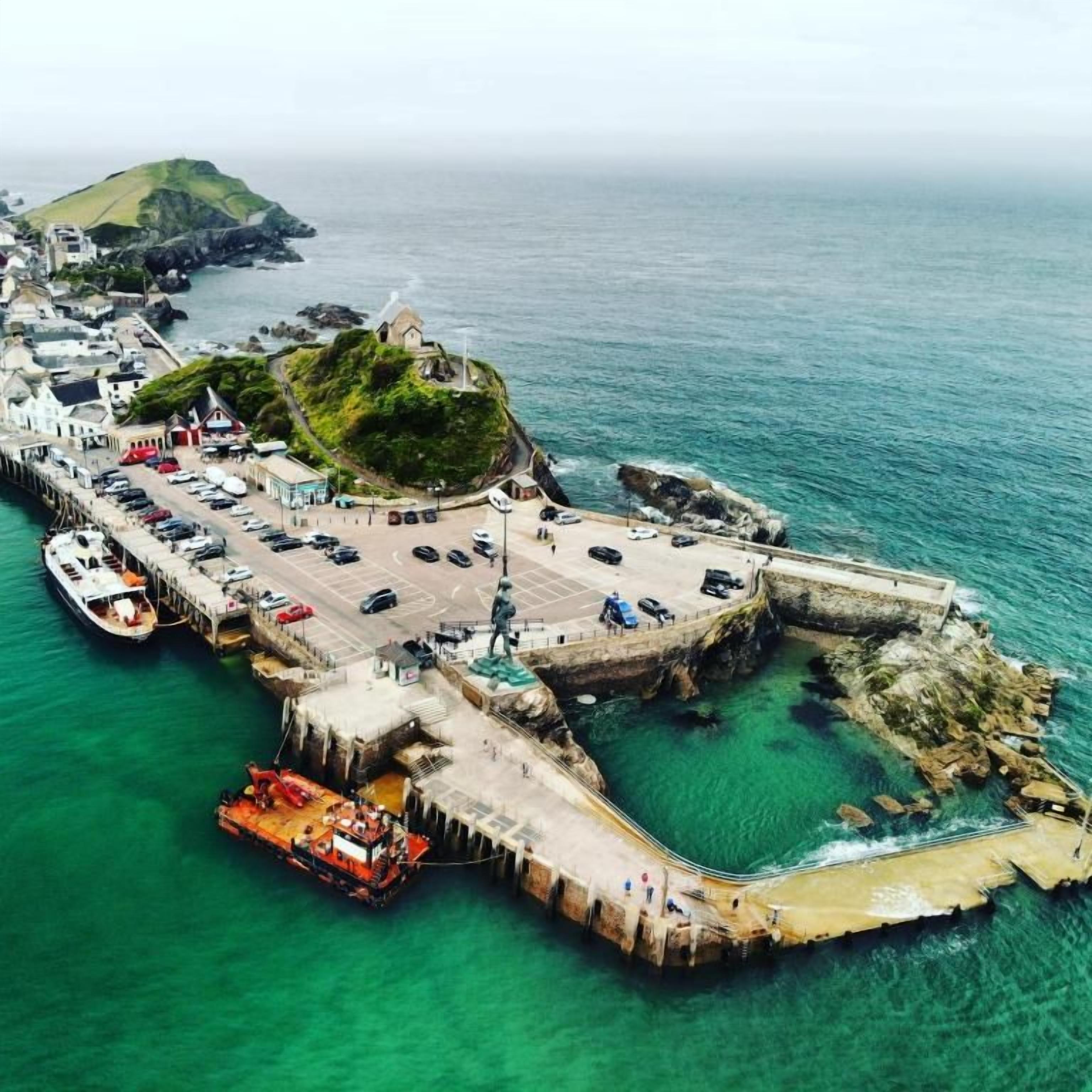 A coastal town with a pier, boats, and a small island with greenery.