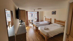 A hotel room with two wooden beds, a desk with a chair, a small table, and a mirror. - The Grand Harbour Hotel (Ilfracombe)