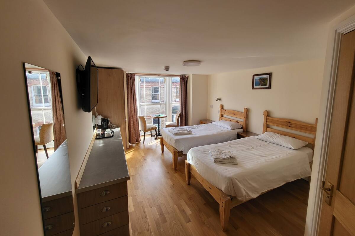 Ein Hotelzimmer mit zwei Holzbett, einem Schreibtisch mit Stuhl, einem kleinen Tisch und einem Spiegel.