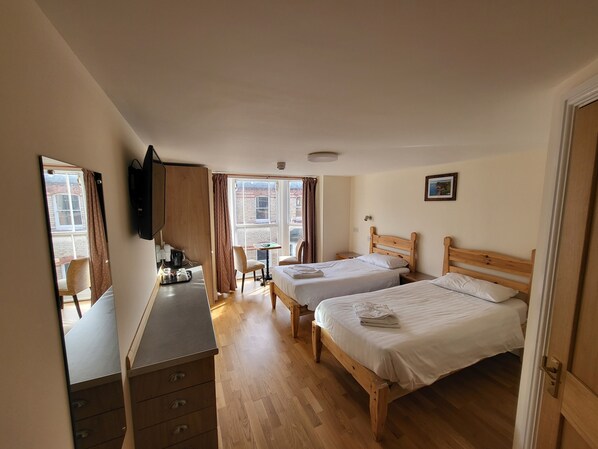 Habitación de hotel con dos camas de madera, un escritorio con una silla, una mesita y un espejo.