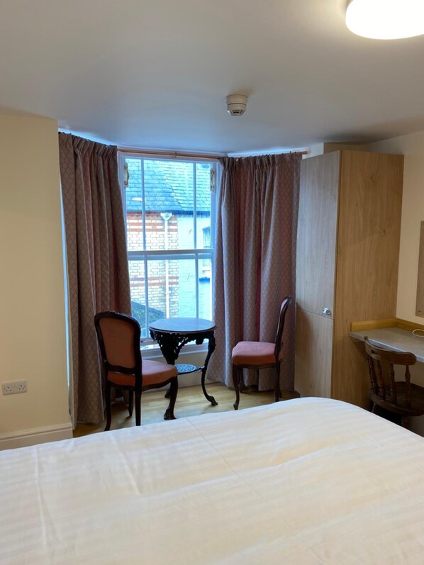 A hotel room with a bed, a small table, two chairs, a window with curtains, and a wardrobe. - The Grand Harbour Hotel (Ilfracombe)
