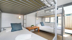 A bunk bed room with a wooden table, white bedding, and a view through a window.