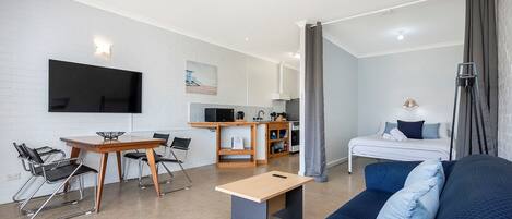 A modern, compact living space with a kitchenette, a dining area, a sofa, and a bed.