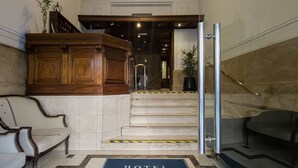 Un vestíbulo de hotel con piso de mármol, un mostrador de recepción, una escalera y una alfombra azul con la inscripción 'HOTEL MARBELLA'.