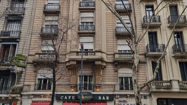 Un edificio de varios pisos con un café o bar en la planta baja, que cuenta con amplias ventanas y balcones ornamentados.