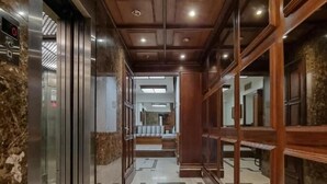Un pasillo con piso de mármol, paneles de madera en las paredes y un ascensor a la izquierda.