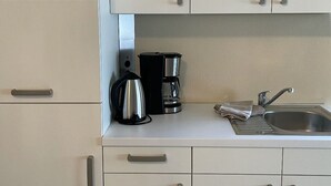 A modern kitchen with white cabinets, a stainless steel sink, and a coffee maker. - 1a apartment Sturm (Emmerthal)