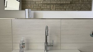 A bathroom with a white sink, a mirror, and a stone backsplash. - 1a apartment Sturm (Emmerthal)