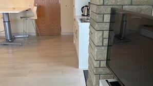 A modern kitchen with a stone fireplace, a flat-screen TV, and a dining area with a wooden door. - 1a apartment Sturm (Emmerthal)