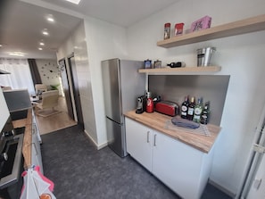A modern kitchen with a stainless steel refrigerator, a wooden countertop, and a shelf with kitchenware.