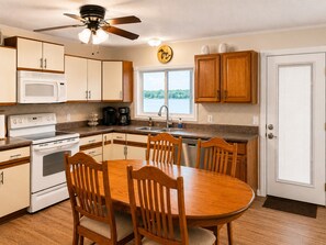 A kitchen with a dining table, chairs, a microwave, stove, and a clock on the wall. - Waterfront Escape on Crooked Lake - Kayaks & Boat Slip. Near Boyne Highlands! (Harbor Springs)