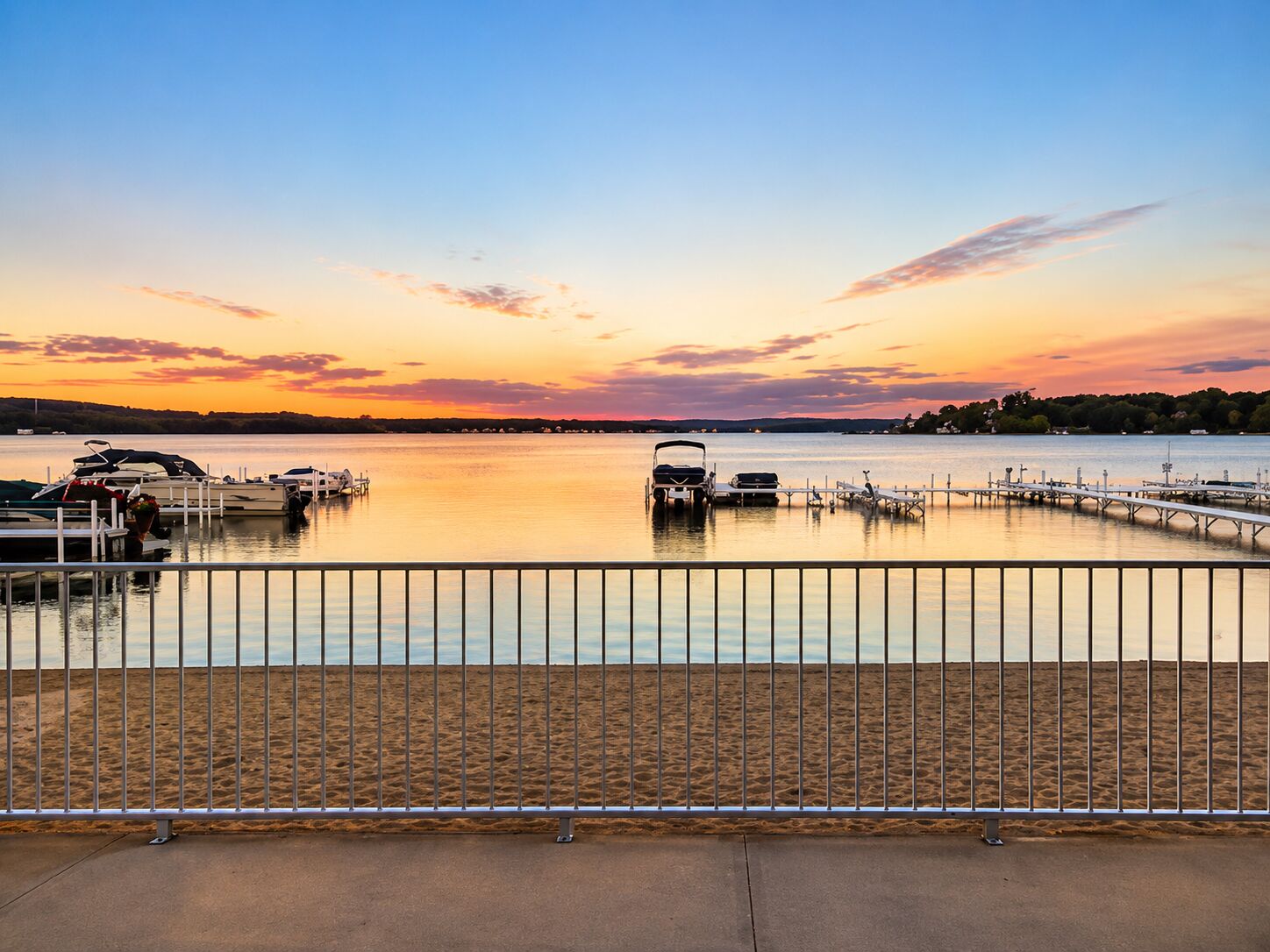 A waterfront marina with boats docked, a pier extending into the water, and a sandy beach area.