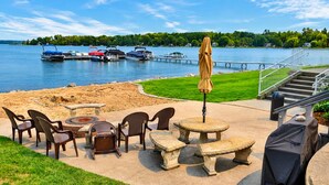 A lakeside patio with outdoor seating, a grill, and boats docked in the background.